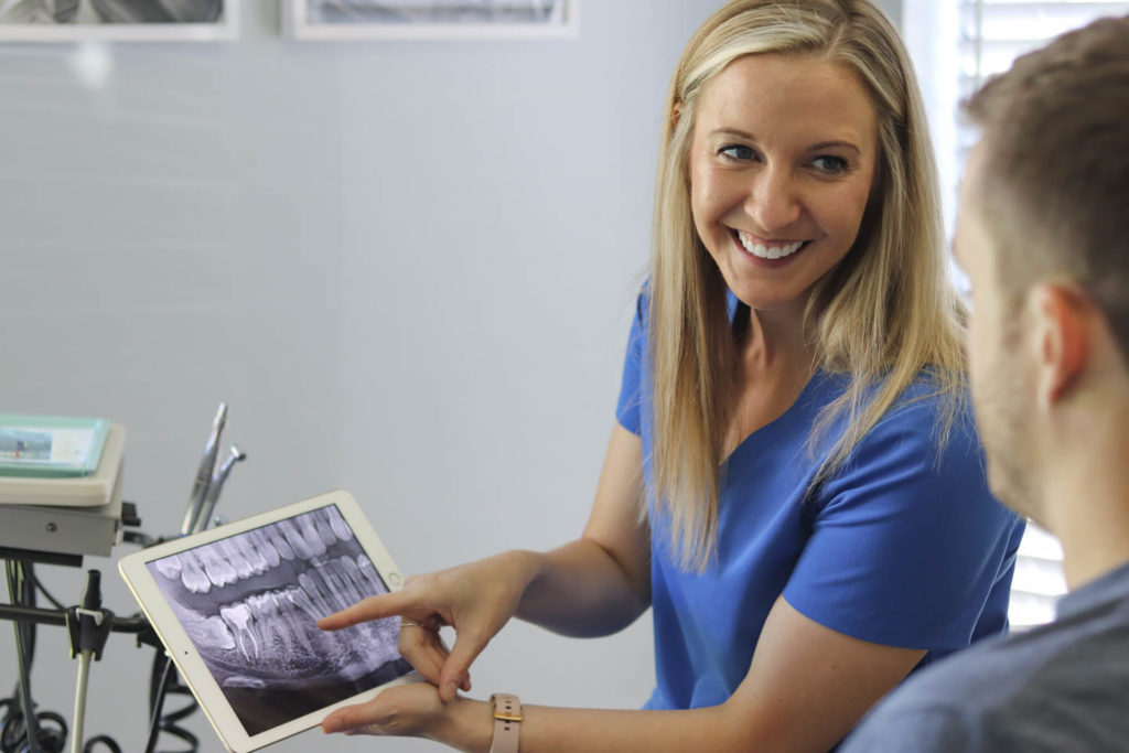 Dr. Ashley Humlicek holds an iPad and discusses dental x-rays with a patient