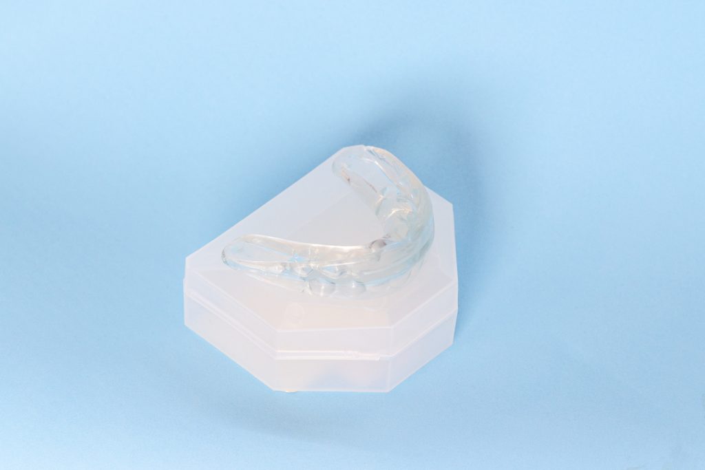 A clear mouth guard sitting on a white protective case on a light blue background