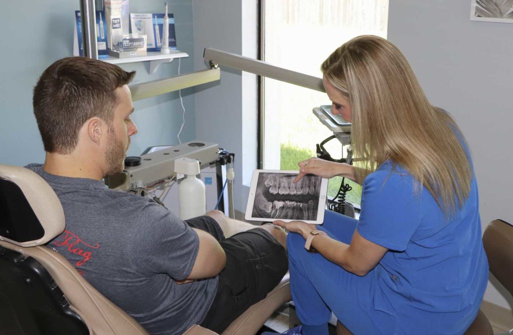 Dr. Ashley Humlicek holds an iPad and discusses dental x-rays with a patient