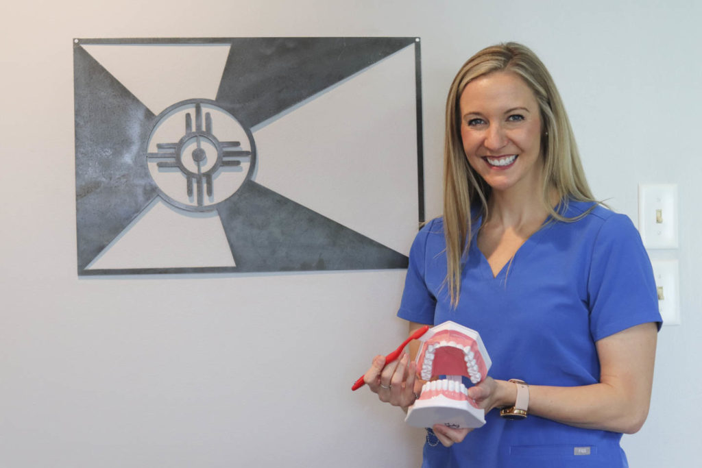 Dr. Ashley Humlicek holding a model of a full set of teeth and a toothbrush
