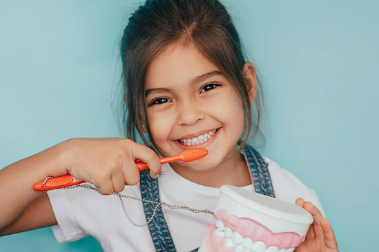 Young girl holding a toothbrush and smiling.