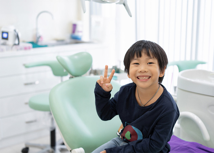 kid smiling while throwing up the peace sign sitting on a dental chair
